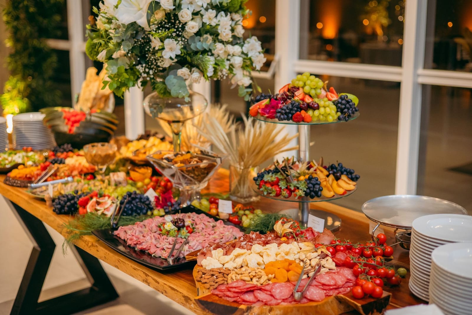 Mesa de antepasto com frios, queijos, castanhas e frutas, decorada com flores brancas